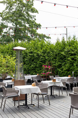 Outdoor cafe terrace with empty tables, white tablecloths, garden greenery and string lights.