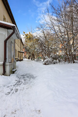 Snow-covered residential alley with icy path and bare trees in winter. 