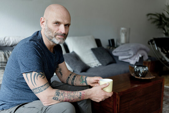 Tattooed man at home sitting on couch, drinking coffee