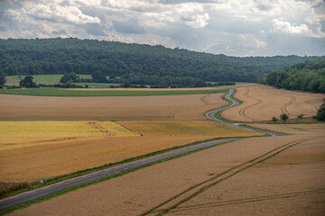 Fototapeta premium Reims, France - 06 26 2025: Panoramic view of cultivated fields with graphical lines, a winding road, trees and hills along the railway line