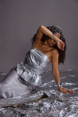 Vertical shot of young adult multiethnic woman sitting on metallic surface, covering face with arm,...