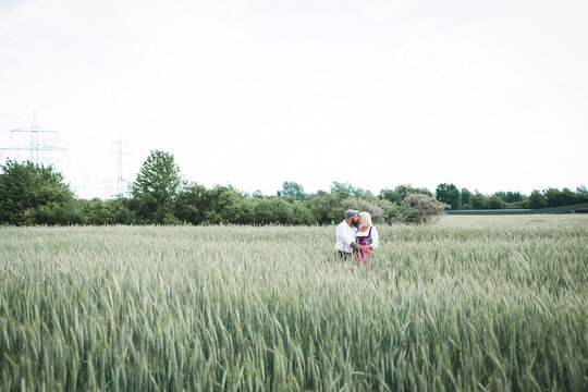 Mature couple kissing while standing amidst plants on landscape against clear sky