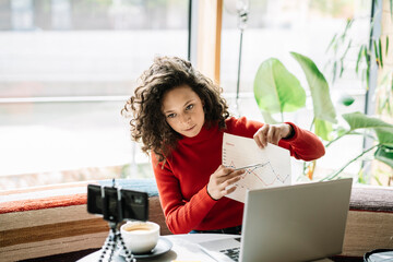 Female influencer showing graph during video call at cafe