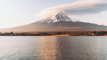 View of Mount Fuji's snow-capped peak reflected on the tranquil lake surface, bathed in the warm glow of the setting sun, Fujikawaguchiko, Yamanashi, Japan.