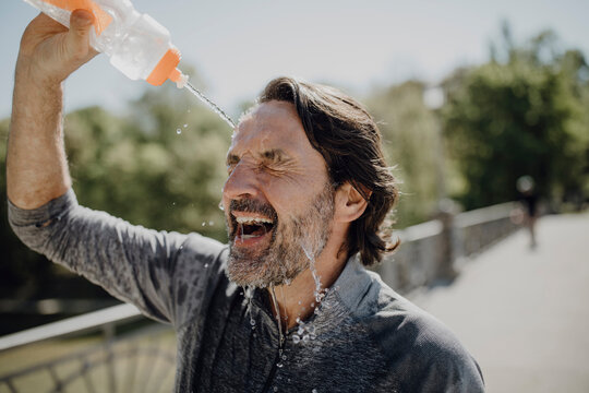 Close-up of mature man pouring water on face in park during sunny day