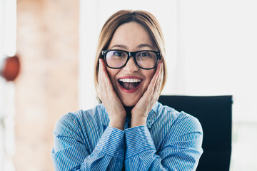Excited professional woman in an office setting expressing surprise and delight wearing glasses and...