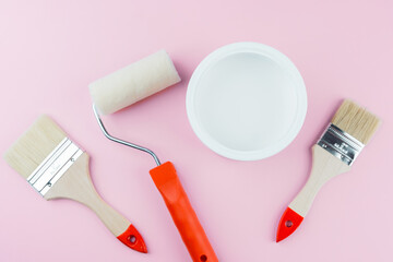 Painting supplies with brushes and roller on pink background for DIY and interior decor concept