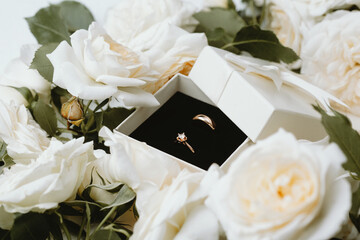 Gold wedding and engagement rings in box surrounded by white roses