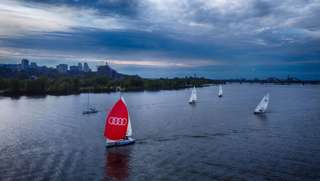 Dnipro, Ukraine - 25 September 2021: Aerial view of sailboats gliding across the Dnipro River under a dramatic sky, the city skyline a distant silhouette.