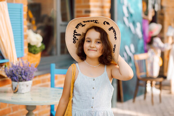 Cute child girl in straw hat in outdoor cafe with oranges fruits. Provence