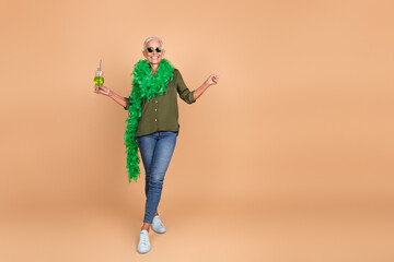 Stylish elderly woman in casual attire posing confidently against a beige background with...