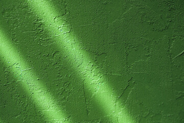 Green stucco wall surface with sunlight and shadows creating abstract texture patterns