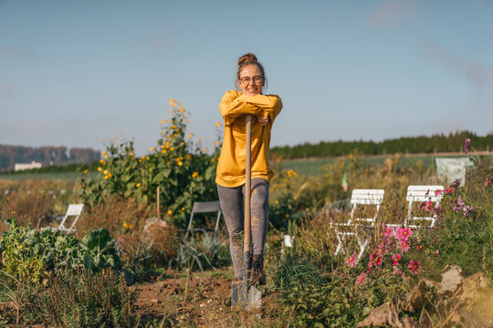 Smiling young woman with spade in cottage garden