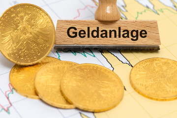 Ein Holzstempel ist beschriftet mit dem Aufdruck Geldanlage vor einigen echten Goldmünzen