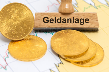 Ein Holzstempel ist beschriftet mit dem Aufdruck Geldanlage vor einigen echten Goldmünzen