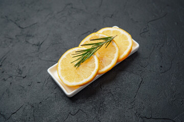Lemon slices with rosemary in small white dish on dark stone background