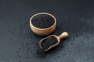 Black sesame seeds in bowl and scoop on dark background