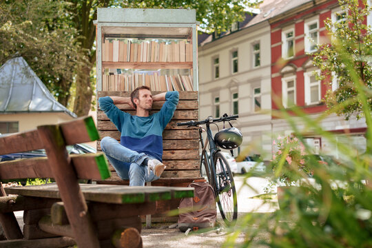 Contemplative man leaning on cabinet with books near bicycle