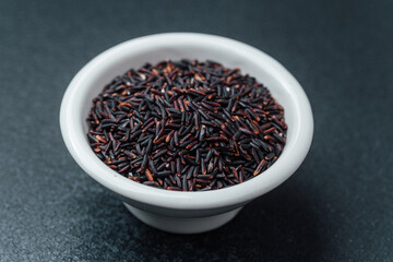 Black rice in white bowl on dark background with loose grains