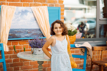 Cute child girl sits in outdoor cafe with oranges fruits. Provence.