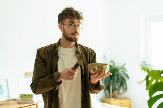 Handsome young man with singing bowl standing in bedroom at home