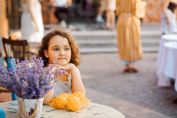 Cute child girl sits in outdoor cafe with oranges fruits. Provence.