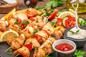 Grilled chicken skewers with vegetables served alongside fresh sauces and sliced salad on a rustic wooden table