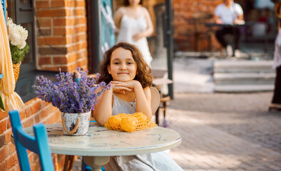 Cute child girl sits in outdoor cafe with oranges fruits. Provence.