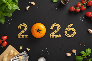 Pasta shaped into 2026 with a yellow tomato as zero surrounded by garlic, basil, cheese, and cherry tomatoes on black background