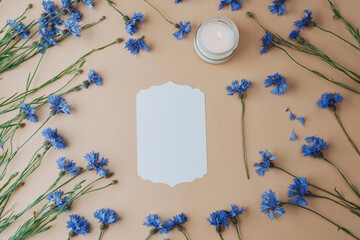 Card with candle and cornflowers on beige background
