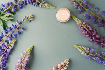Candle and lupine flowers frame on green background