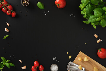 Frame made of fresh Italian ingredients such as cherry tomatoes, garlic, basil, cheese, salt, and pepper on a black background. Space for your text.