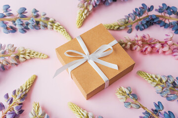 Gift box and lupin flowers on pink background with space for text