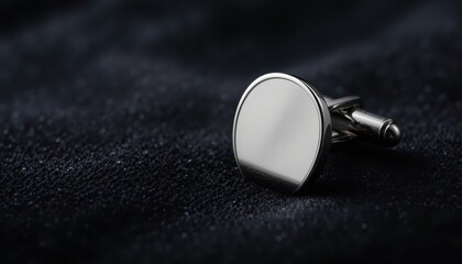 Elegant silver cufflink with a polished surface on a dark textured background with copy space
