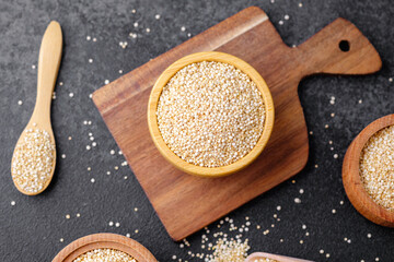 Quinoa seeds in multiple wooden bowls and spoons on dark background