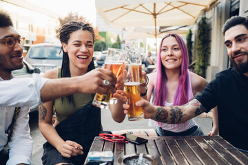 Happy friends clinking beer glasses outdoors at a bar