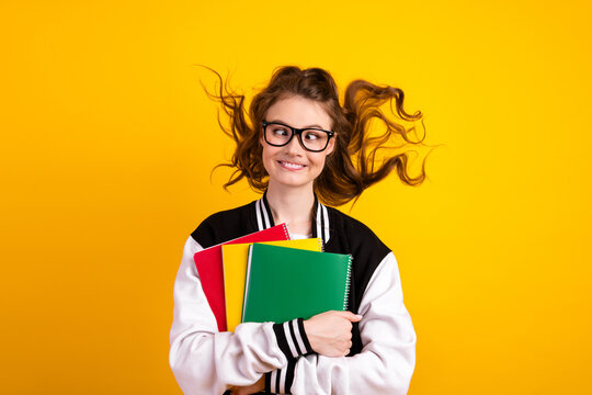 Smiling young student holding colorful notebooks in a casual outfit on a bright yellow background