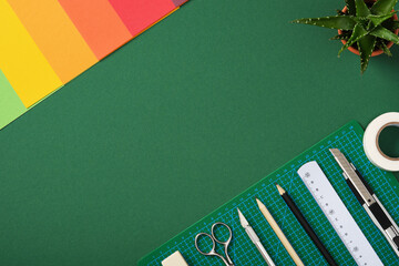 Top view of the paper crafts work table. Stationery supplies and colorful paper arranged on a green background with copy space.