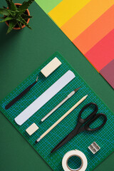 Top view of the paper crafts work table. Stationery supplies and colorful paper arranged on a green background.