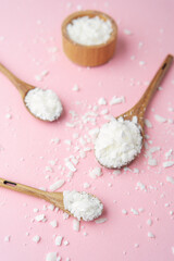 Multiple wooden spoons with soy wax flakes on pastel pink background