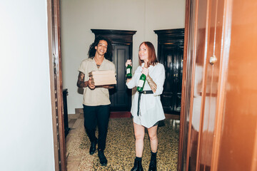 Friends with beer bottle and pizza boxes at entrance of home