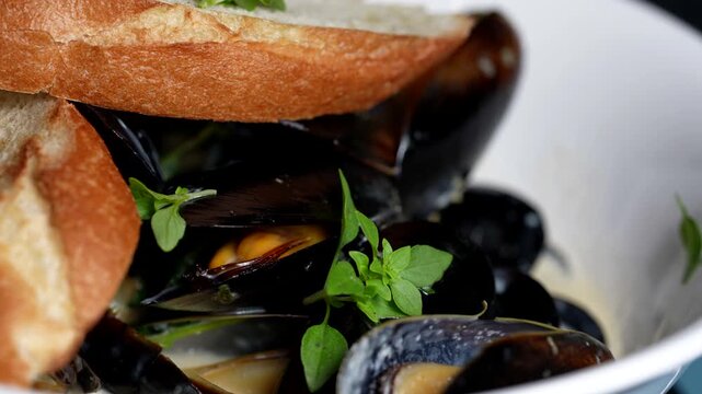 Steamed black mussels in creamy broth, garnished with fresh herbs, served with crispy baguette slices.