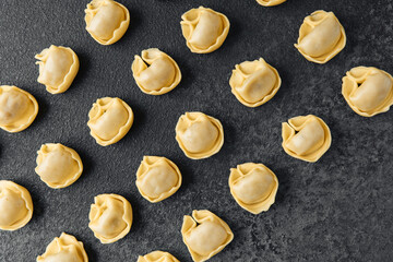 Diagonal scattered raw cappelletti pasta on dark background close up