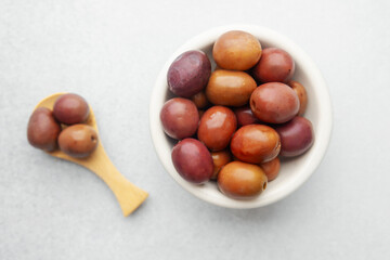 Kalamata olives in white bowl and wooden spoon on bright background