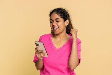 Indian woman happily looks at smartphone screen, celebrating exciting online news. Arabian girl on...