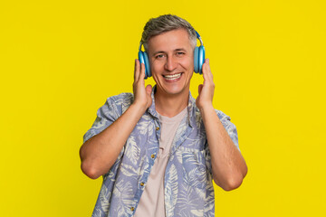 Middle-aged man dancing with wireless headphones on, moving to rhythm and smiling with pure joy,...