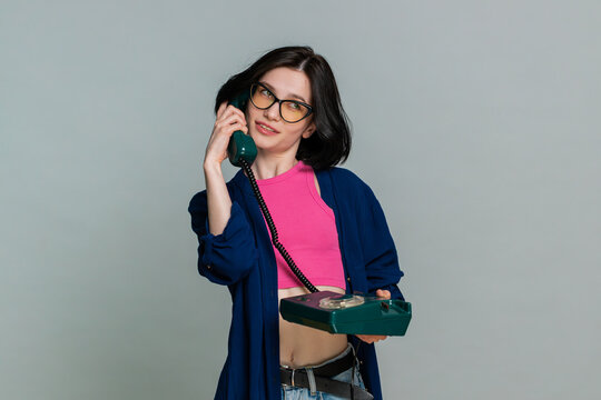 Young woman emotionally speaks into a retro wired telephone actively explaining something, expressive reaction gestures. Girl demonstrates engaging conversation and emotion isolated on gray background - Powered by Adobe