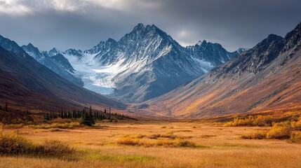   A snow-capped mountain range stands tall against a backdrop of lush green trees and golden grass