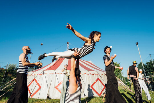Male and female acrobats performing with artists in front of circus tent