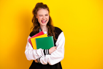 Confident Teen Student Winking and Holding Colorful Notebooks on a Vibrant Yellow Background